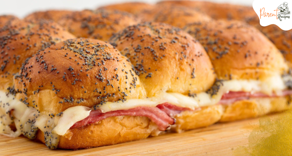 Close-up of gooey baked ham and cheese sliders with golden-brown tops.